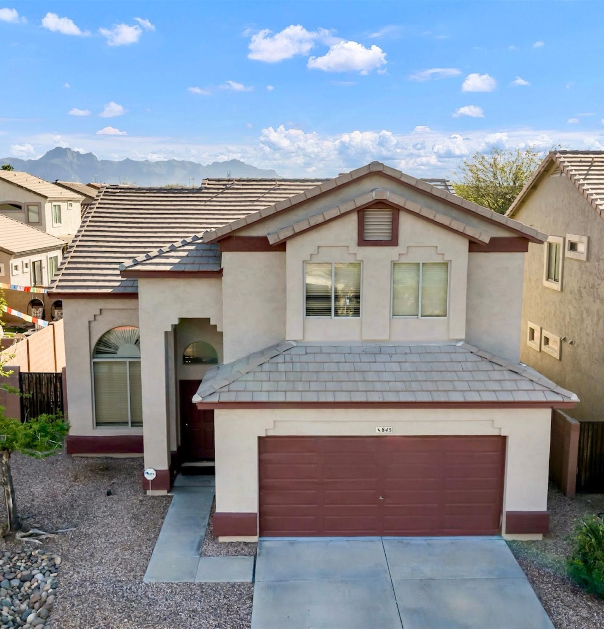 Front exterior view of 845 S Cerise in Mesa, AZ, featuring a modern two-story design with tan stucco, stacked stone pillars, a two-car garage, and professional desert landscaping within the gated La Fortina HOA.