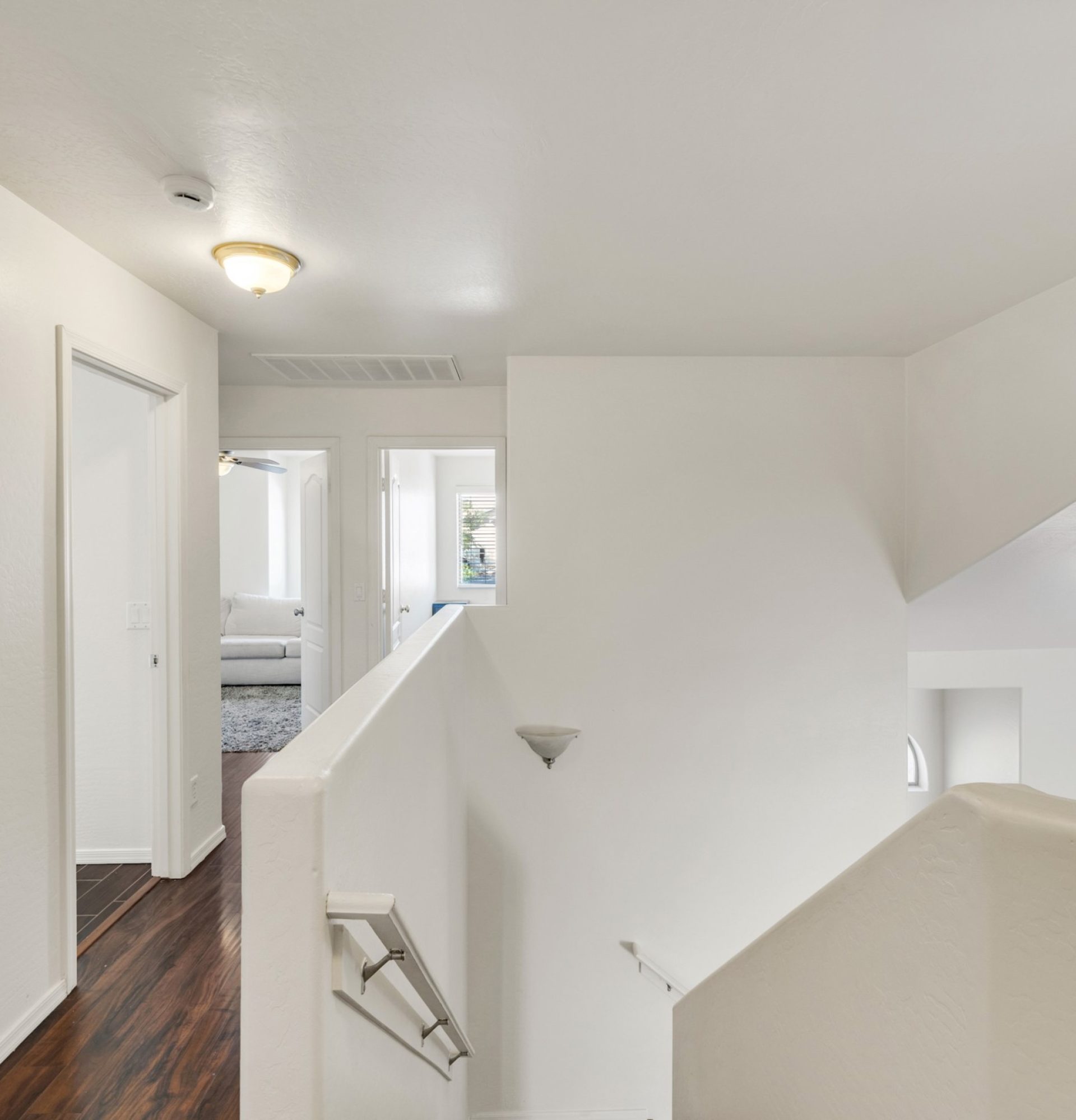 View of the second-floor landing and hallway at 845 S Cerise in Mesa, AZ, featuring dark wood flooring, white walls, a vaulted ceiling, and a glimpse into a spacious bedroom in the gated La Fortina community.