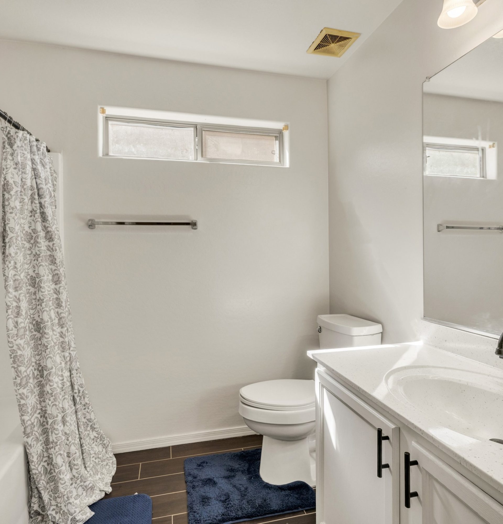 Interior of the full guest bathroom at 845 S Cerise in Mesa, AZ, featuring a white vanity with matte black hardware, a large mirror, a bathtub and shower combination with a patterned curtain, and dark wood-look tile flooring in the gated La Fortina community.