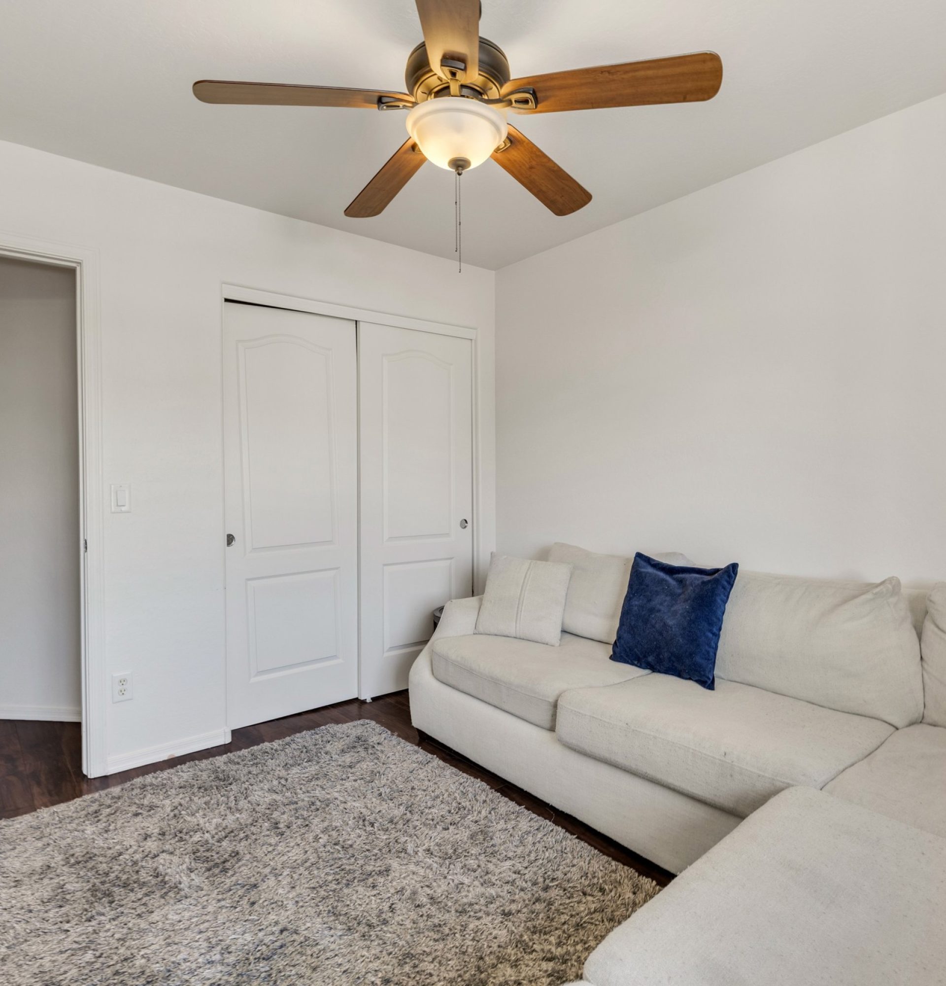 Interior view of a spacious bedroom at 845 S Cerise in Mesa, AZ, currently used as a home office, featuring neutral grey carpet, soft white walls, a large window with blinds, and a modern ceiling fan in the gated La Fortina community.