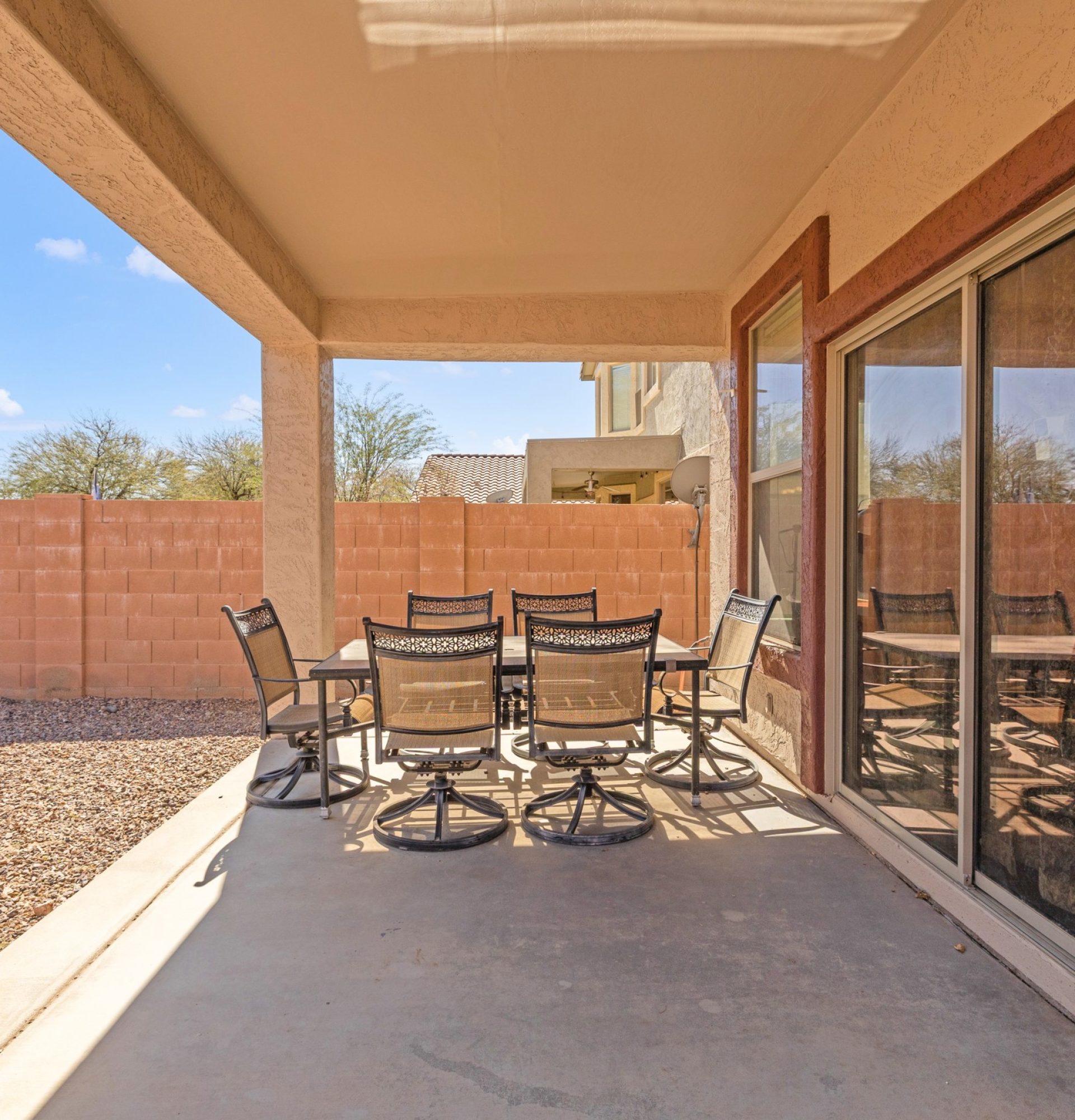 View from the covered patio at 845 S Cerise in Mesa, AZ, looking out toward a low-maintenance gravel backyard and privacy wall, featuring a sliding glass door and outdoor dining set in the gated La Fortina community.
