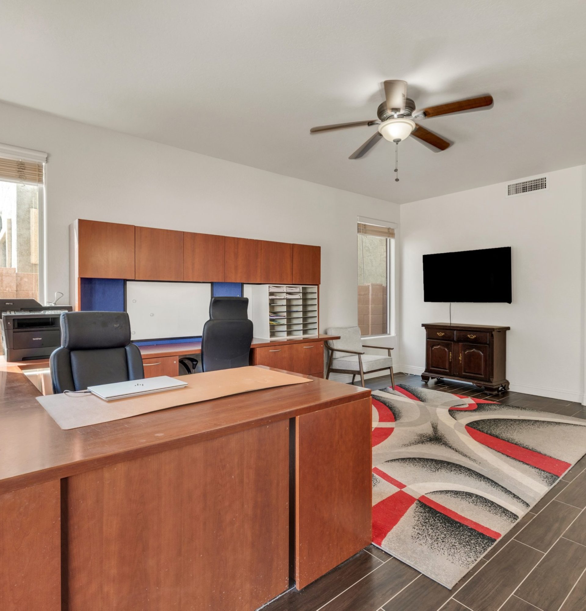 Interior view of a spacious multipurpose room at 845 S Cerise in Mesa, AZ, featuring modern wood-look tile flooring, neutral white walls, a stylish ceiling fan, and large windows overlooking the side yard in the gated La Fortina community.